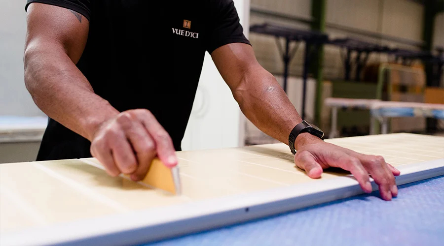 Artisan menuisier travaillant sur un panneau de volet polyuréthane monobloc dans l'atelier Vue d'ici